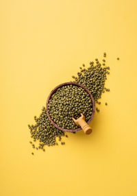 Mung beans top view on yellow background, minimal style. wooden bowl with green mung beans