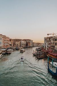 Buildings by canal in city against clear sky during sunset