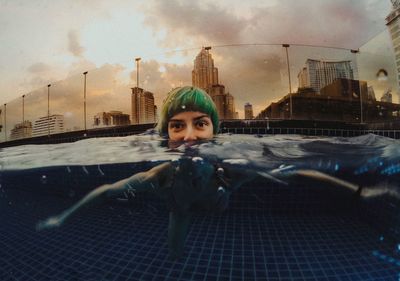 Portrait of young woman with dyed hair swimming in pool against sky during sunset