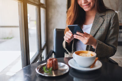 Midsection of businesswoman using mobile phone at coffee shop