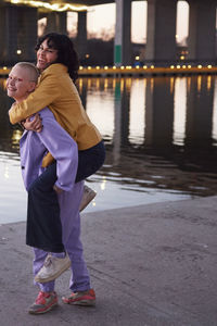 Young woman giving friend or girlfriend piggyback ride, man taking photo