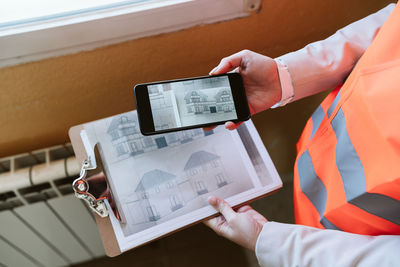 Unrecognizable architect woman in construction site using mobile phone holding blueprints