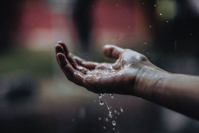 Cropped hand under falling water outdoors