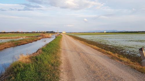 Empty road amidst field against sky