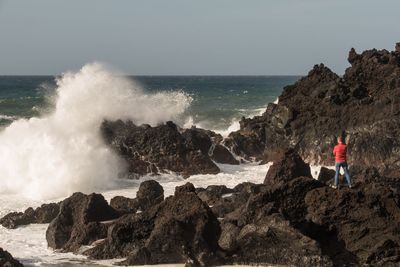 Man standing on rock by sea against clear sky