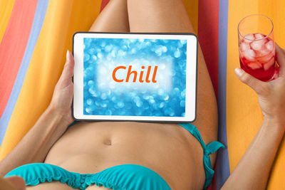 Midsection of bikini woman with drink showing chill message on digital tablet