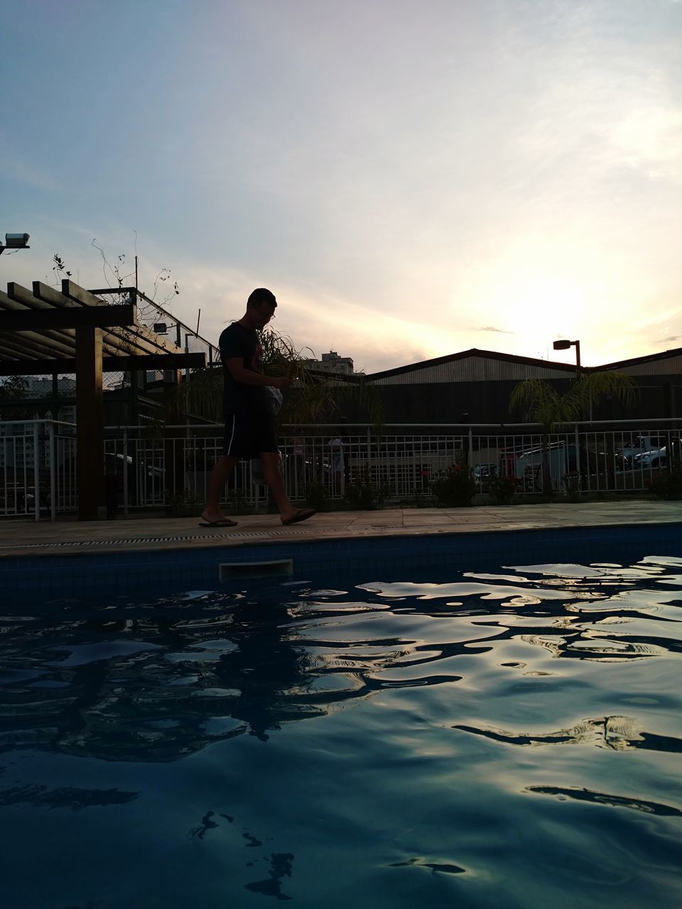 MAN STANDING AT SWIMMING POOL AGAINST SKY