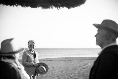 Senior woman holding hat while standing at beach