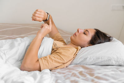 Young woman checking time while lying on bed at home