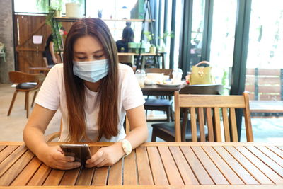 Young woman using phone while sitting on table