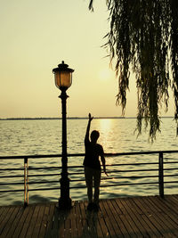 Rear view of silhouette woman standing on pier by sea against clear sky during sunset