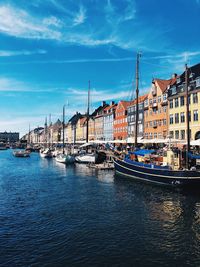 Sailboats moored on river by buildings against sky