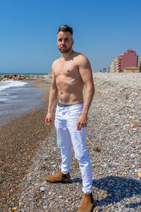 Full length portrait of shirtless man standing on beach