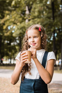 Schoolgirl drinking from an eco-friendly cup and straw in the park. vertical view