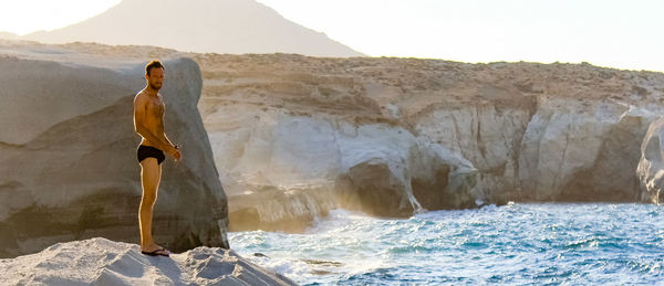 Rear view of man standing on rock by sea against clear sky