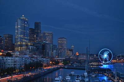 Illuminated buildings and ferris wheel against sky at night in city