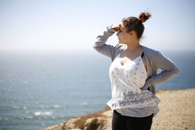 Young woman shielding eyes while standing on cliff