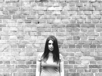 Portrait of young woman standing against brick wall