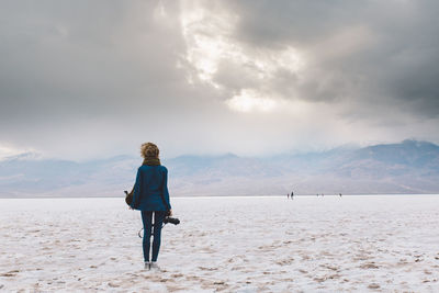 Rear view of woman holding camera standing on snow covered land