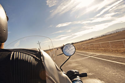 Rear view of man riding motor scooter on road against sky