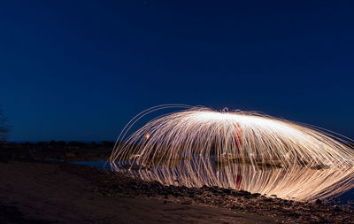 Light trails on beach against clear blue sky at night