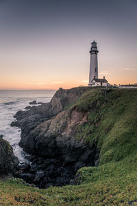 Lighthouse by sea against sky during sunset