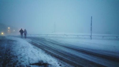 People walking on snow covered landscape against sky