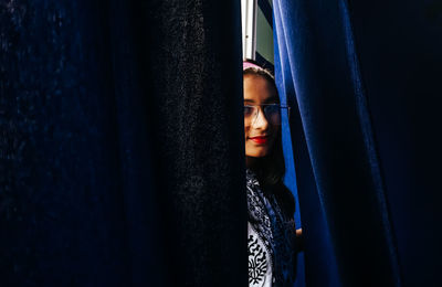 Portrait of smiling teenage girl seen through curtains