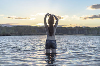 Rear view of shirtless woman standing in lake against sky