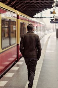 Rear view of man walking at railroad station platform