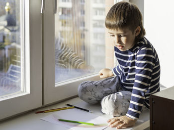 Cute boy studying by window at home