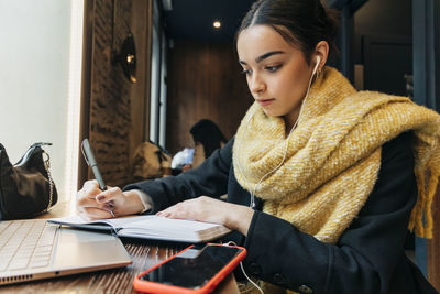 Teenager writing in diary and listening music through earphones