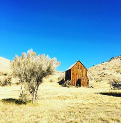 Abandoned house on field against clear blue sky