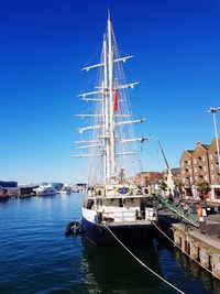 Sailboats moored at harbor against clear blue sky