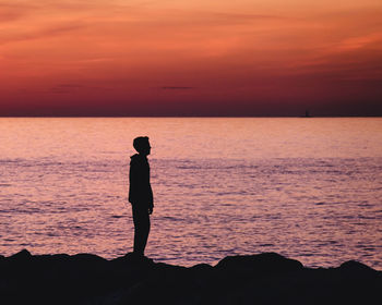 Silhouette man standing at beach against sky during sunset