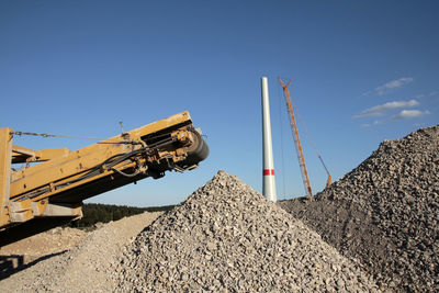 Low angle view of crane at construction site against clear blue sky