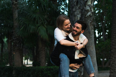 Young couple standing by trees against plants