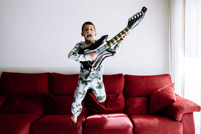 Boy jumping from sofa while playing guitar in living room