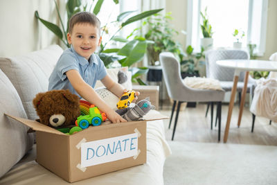 Portrait of boy with teddy bear while sitting on sofa at home