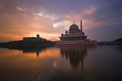 Mosque by lake against sky during sunset