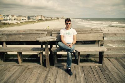 Portrait of young man sitting on bench against sea