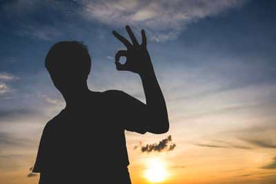 Silhouette man gesturing ok sign against sky during sunset