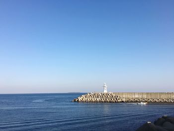 Lighthouse by sea against clear blue sky