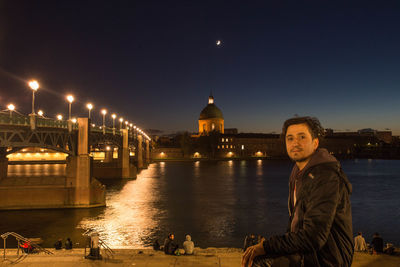 Portrait of young woman standing by river against sky at night