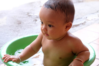 Close-up of shirtless baby boy taking bath in bucket