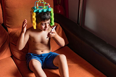 High angle view of shirtless boy sitting on sofa while talking on phone at home