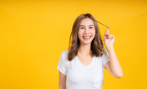 Portrait of smiling young woman against yellow background