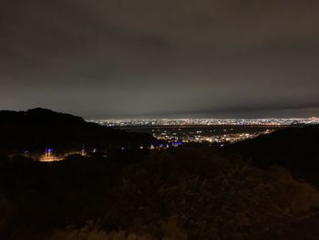 Illuminated city by sea against sky at night