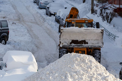 Tractor removing snow from parking near residential building at winter day