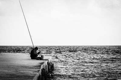 Man fishing in calm sea against clear sky